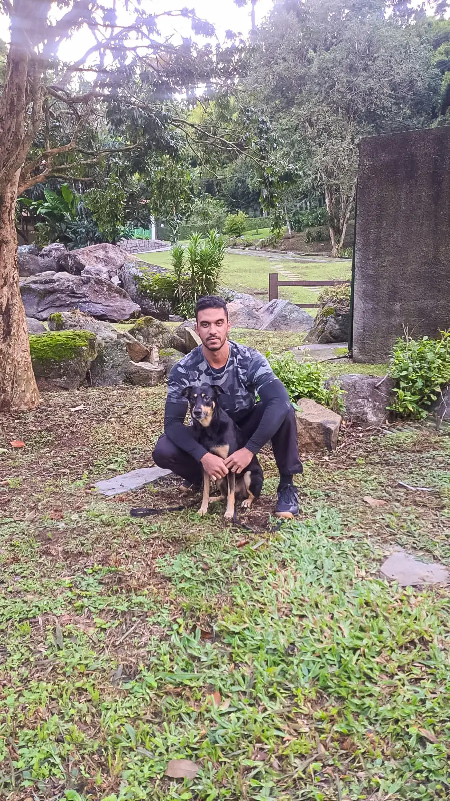 João Ramos agachado no jardim, abraçando o Bolt, seu cão preto e caramelo